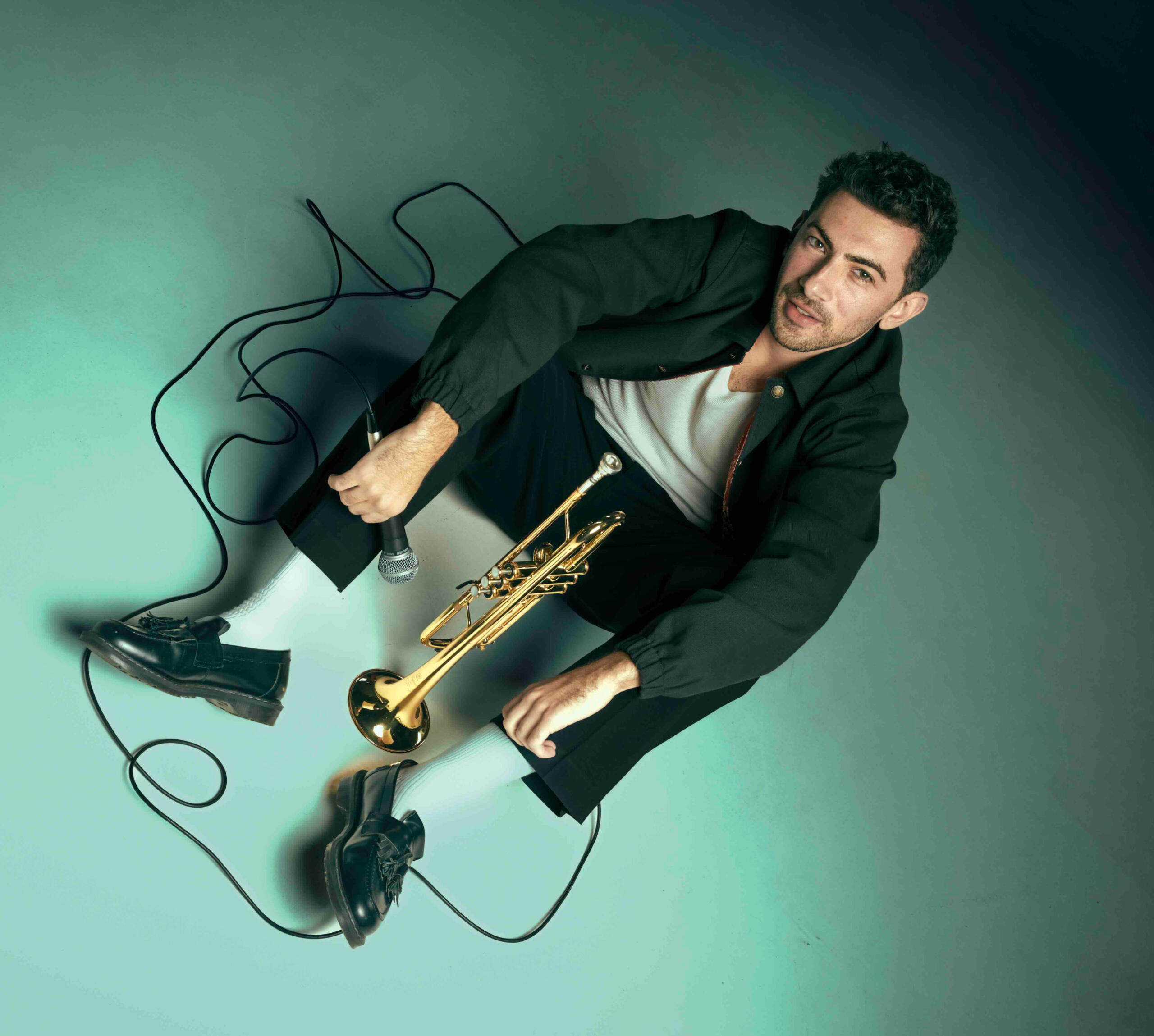 Jacket Trumpet Mic Floor Musician John Dimase sitting on the floor surrounded by his microphone cable. With his trumpet, and holding a microphone.