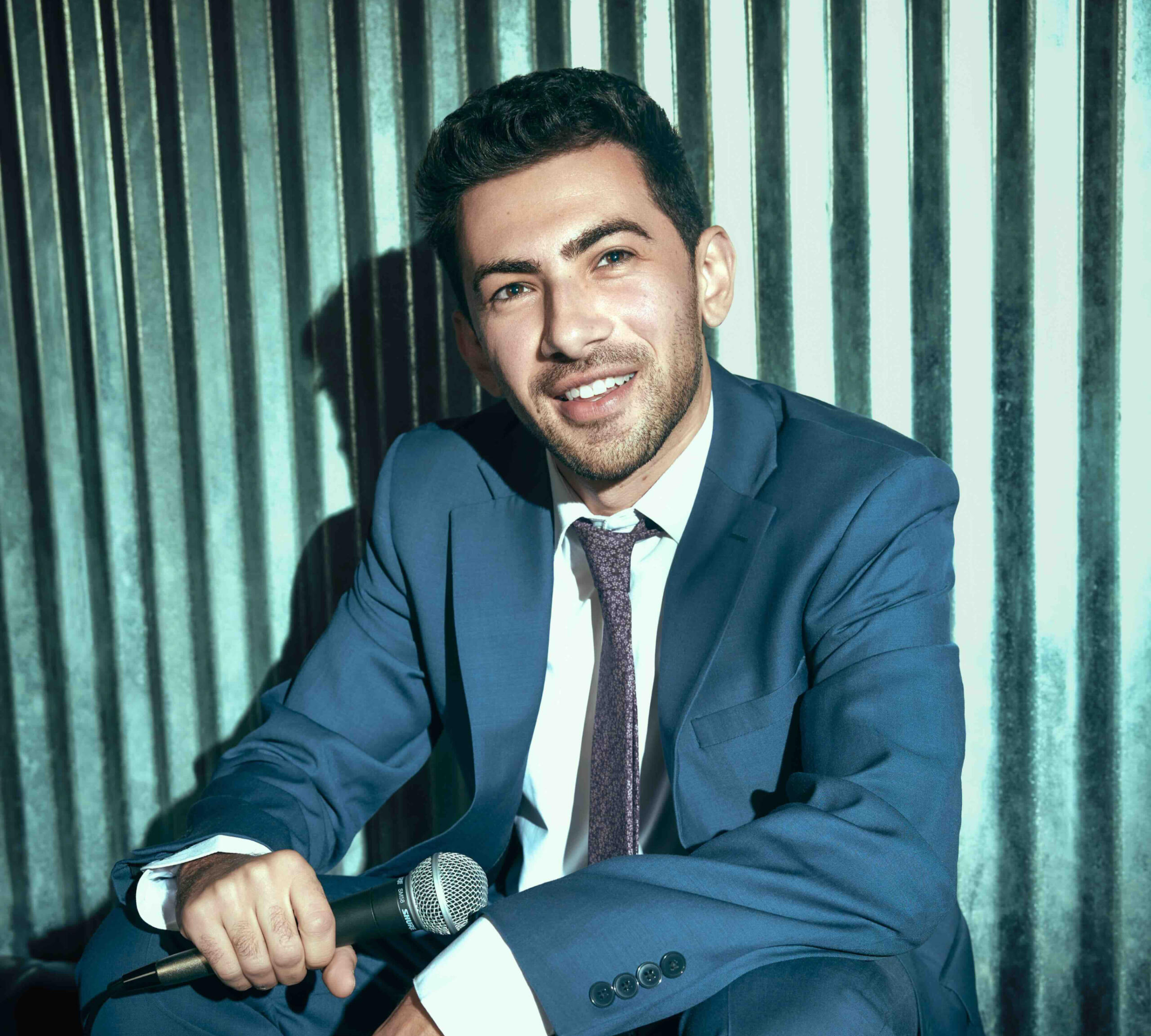 Musician John Dimase smiling while wearing a blue suit, white shirt, purple tie. Metal backdrop and cool color tones make the image "pop".